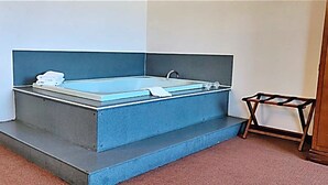 Een moderne badkamer met een groot rechthoekig bad, een klein houten krukje en een zichtbaar raam.