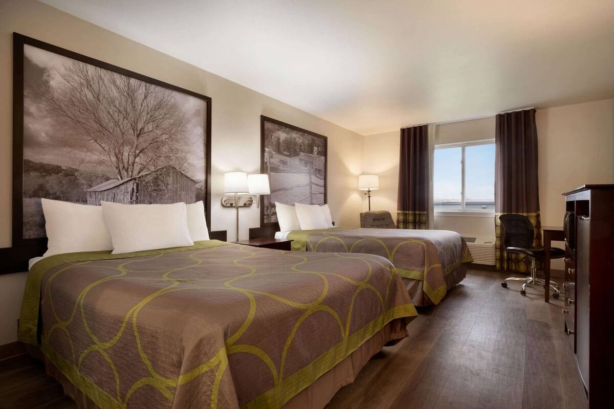 Une chambre d’hôtel avec deux lits, un bureau, une chaise et une grande fenêtre.