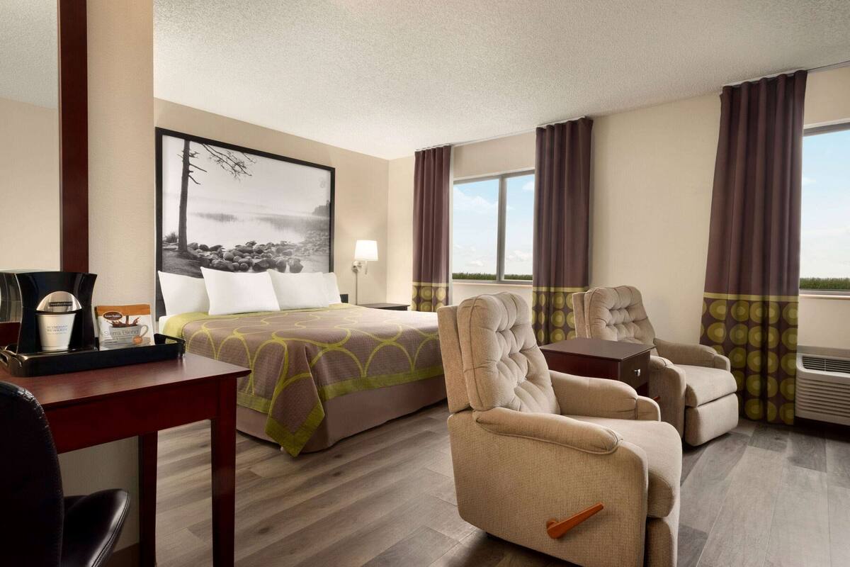 Une chambre d’hôtel avec un lit, une chaise, un bureau et une grande fenêtre avec des rideaux.