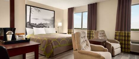 A hotel room with a bed, a chair, a desk, and a large window with curtains.