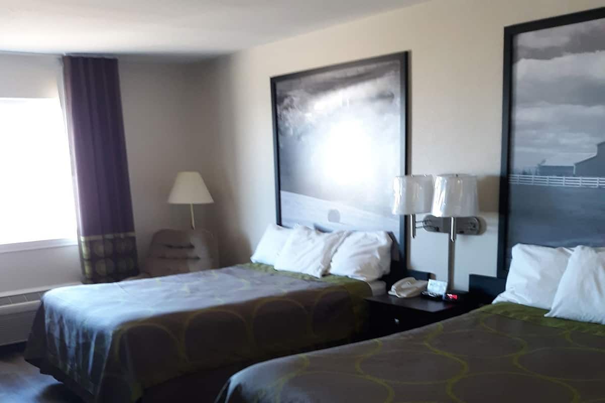 Une chambre d’hôtel avec deux lits, une table de chevet avec une lampe, une fenêtre avec des rideaux et un tableau au mur.