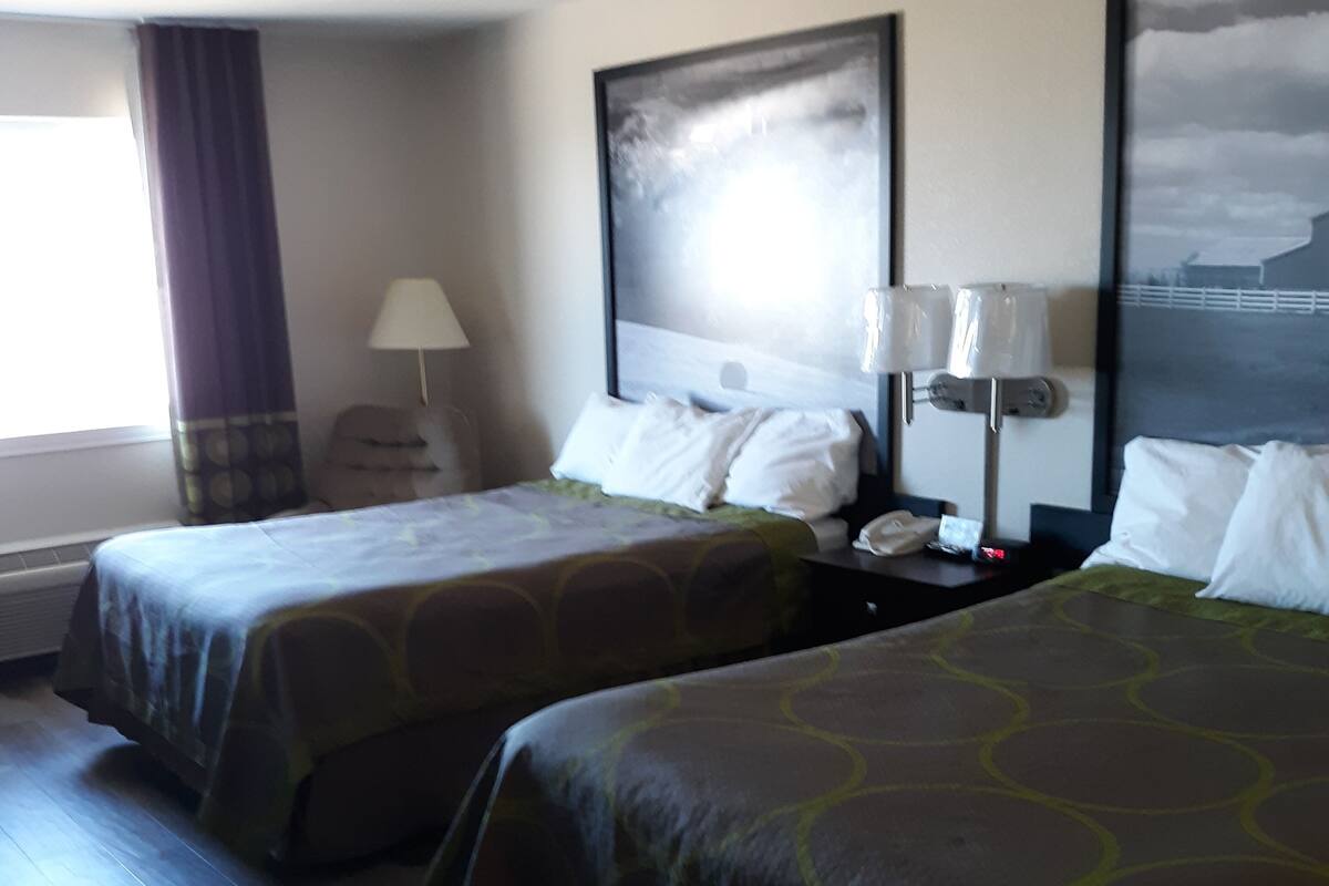Une chambre d’hôtel avec deux lits, une table de chevet avec une lampe, une fenêtre avec des rideaux et un tableau au mur.