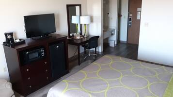 A hotel room with a bed, a desk with a chair, a television, a mini-fridge, and a bathroom visible through an open door.