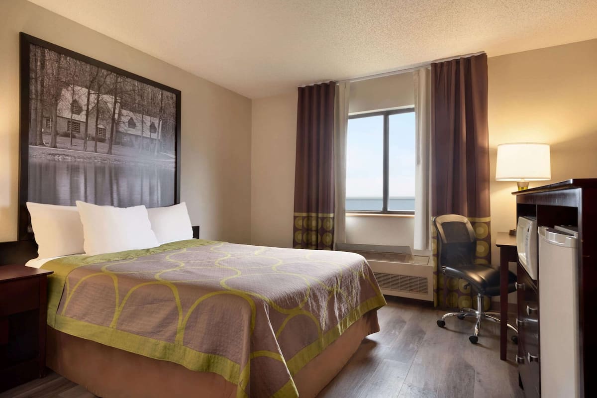 Une chambre d’hôtel avec un grand lit, un bureau avec une chaise, une télévision et une fenêtre avec des rideaux.