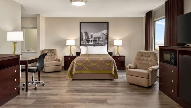 A hotel room with a bed, two armchairs, a desk with a chair, a TV, and a painting on the wall. - Super 8 by Wyndham Bethany MO (Bethany)