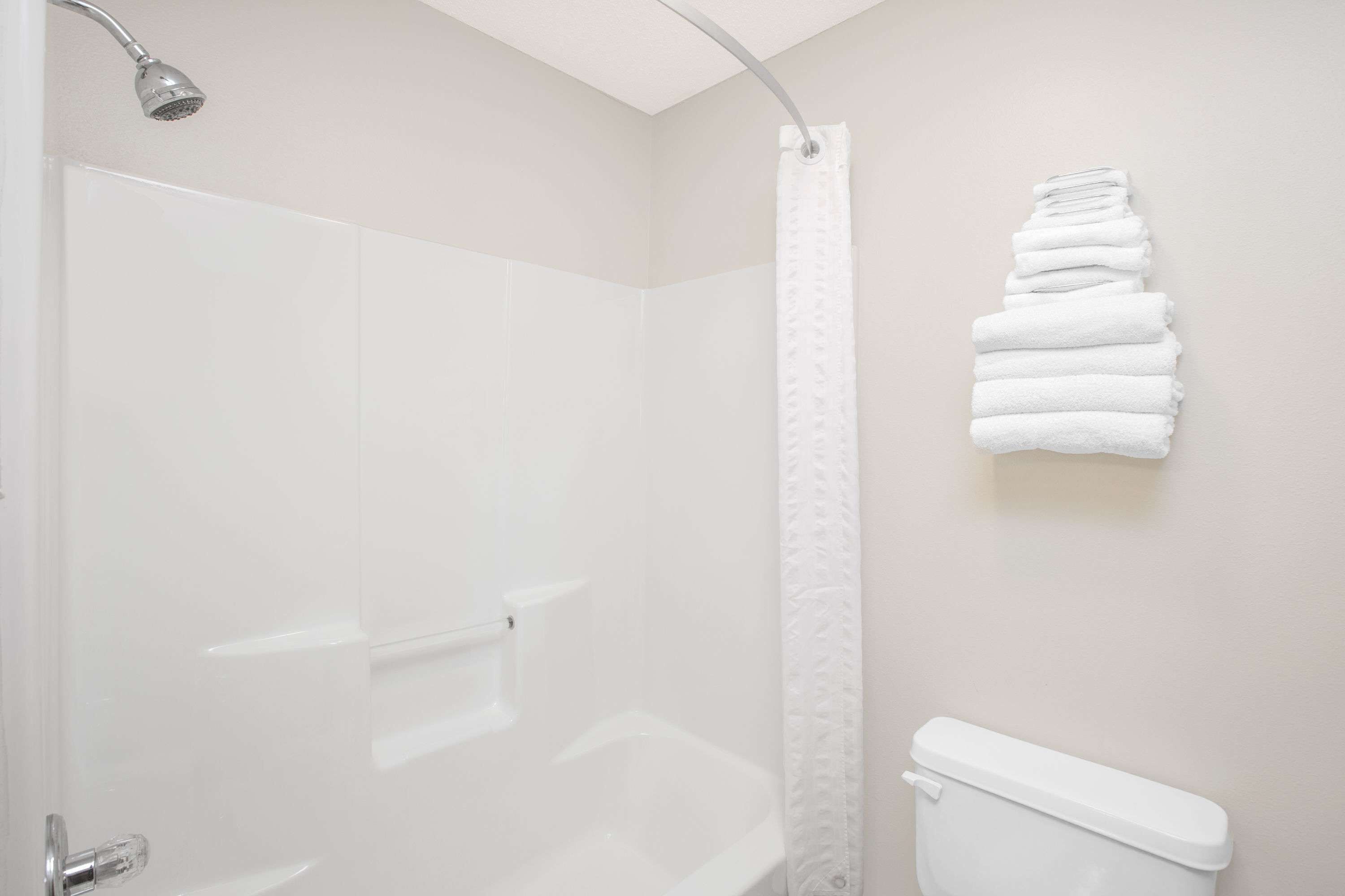 Un baño con ducha, inodoro y una pila de toallas blancas en la pared.