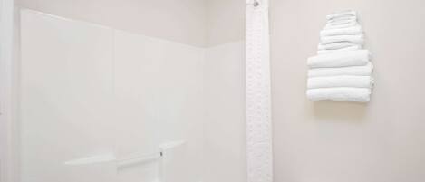 Un baño con ducha, inodoro y una pila de toallas blancas en la pared.