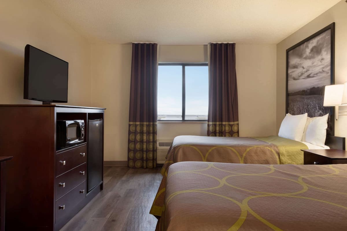 Une chambre d’hôtel avec un lit, un téléviseur posé sur une commode, une fenêtre avec des rideaux et un tableau accroché au mur.