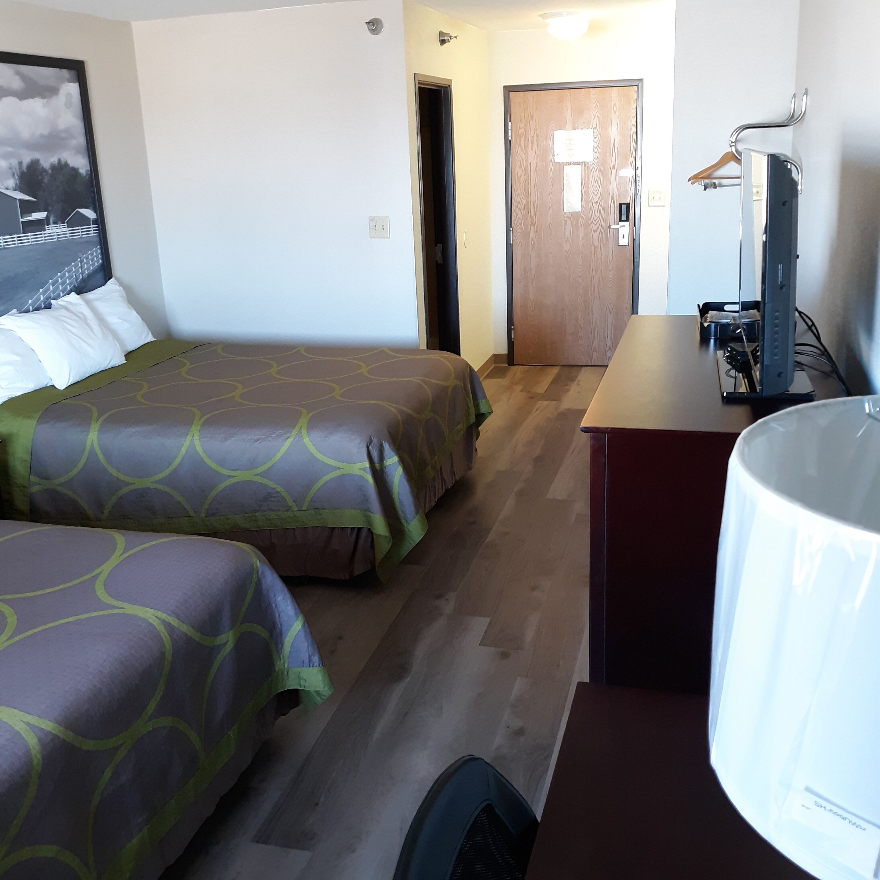 A hotel room with two beds, a desk, a chair, and a television.