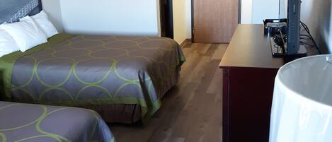 A hotel room with two beds, a desk, a chair, and a television.