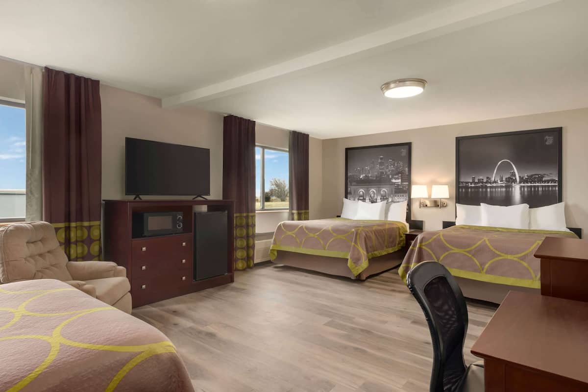 Une chambre d’hôtel avec deux lits, une télévision, un bureau et une chaise. Il y a deux fenêtres avec des rideaux, et des œuvres d’art sont accrochées aux murs.