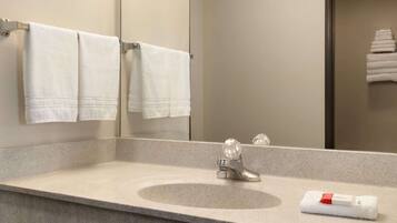 A bathroom with a granite countertop, a sink, and a mirror. There are white towels hanging on a rack and a folded towel on the countertop.
