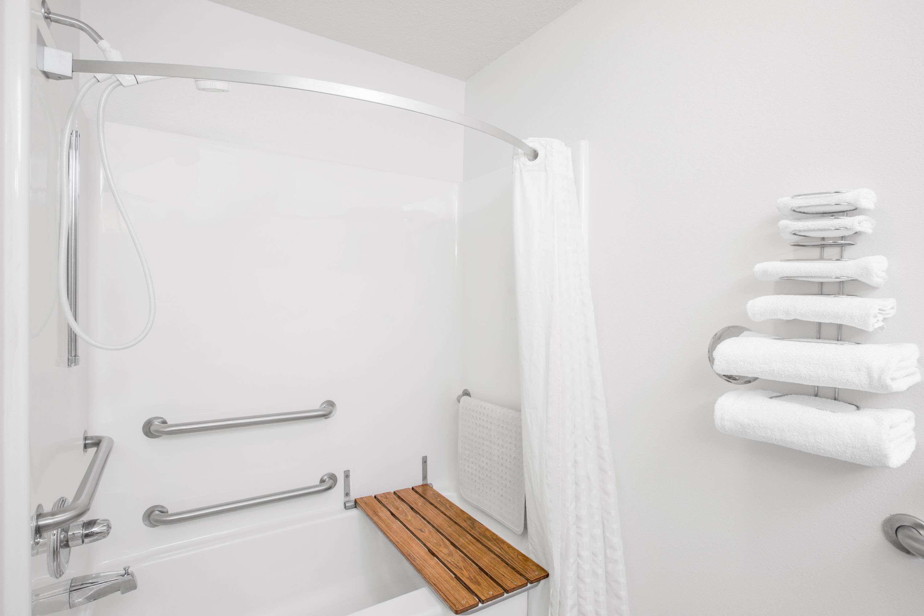 A shower with a glass door, a wooden shelf, and a towel rack with multiple towels.