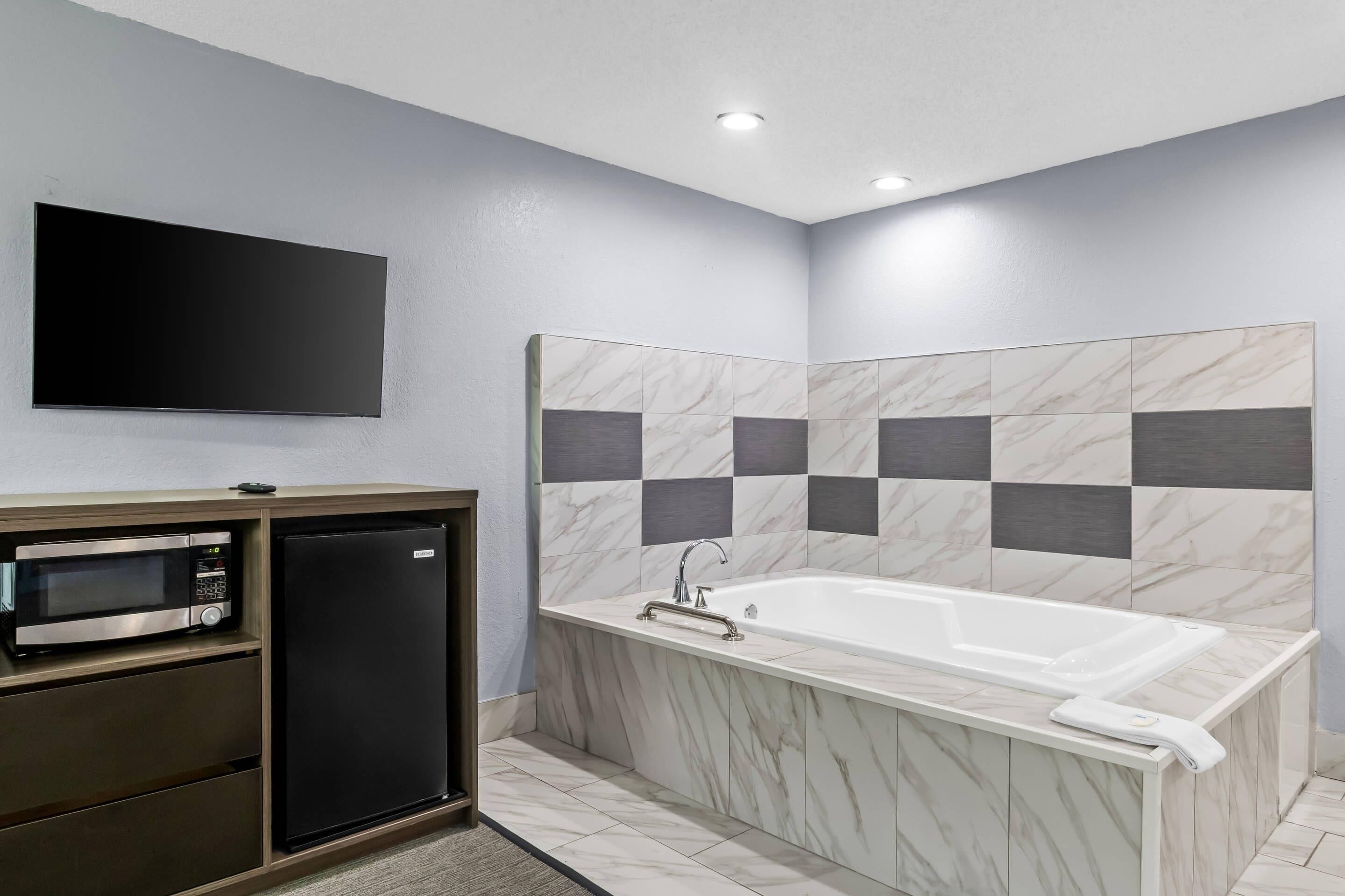 A modern bathroom with a built-in shower, a vanity with a microwave, and a flat-screen TV mounted on the wall.