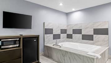 A modern bathroom with a built-in shower, a vanity with a microwave, and a flat-screen TV mounted on the wall.