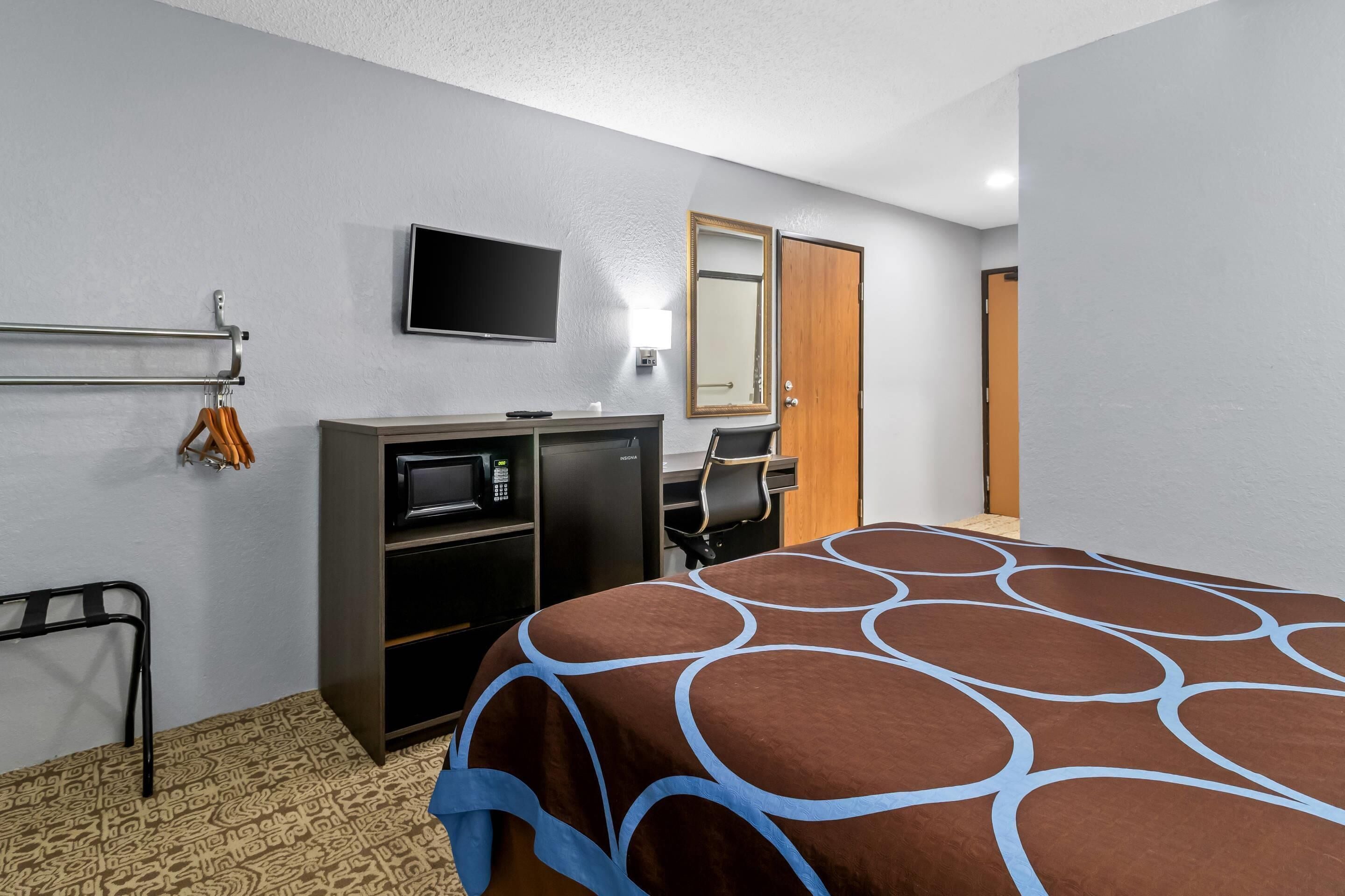 Habitación de hotel con cama, escritorio con silla, televisor, armario y perchero.