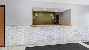 A reception area with a green wall, a wooden counter, and a tiled floor. - Rodeway Inn Delmont (Delmont)