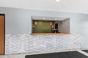 Un área de recepción con una pared verde, un mostrador de madera y suelo de baldosas.