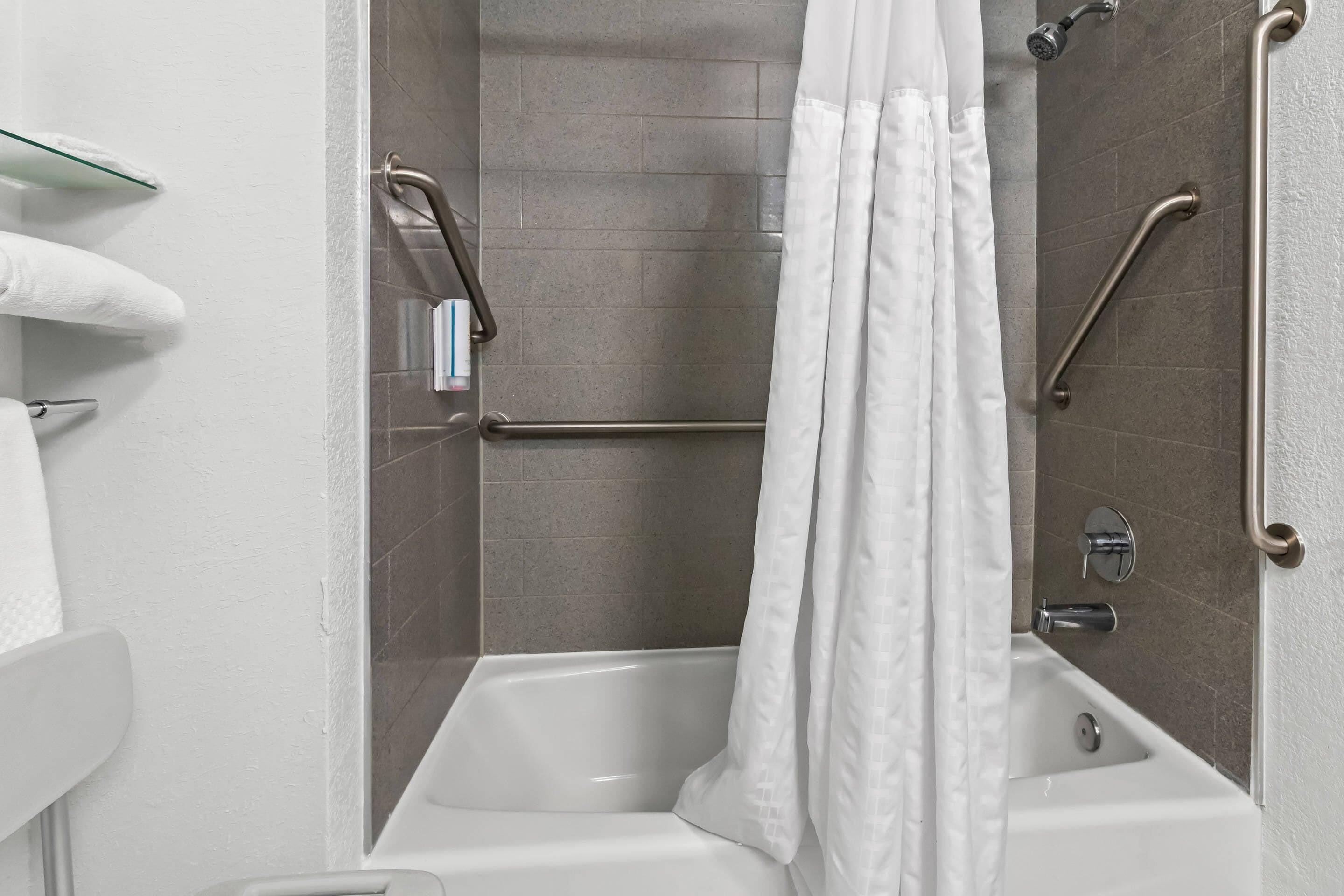 Un baño moderno con bañera, barras de apoyo y cortina de ducha.