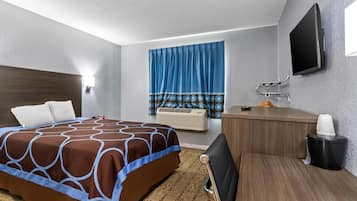 Habitación de hotel con cama, escritorio, silla, televisor y ventana con cortinas.