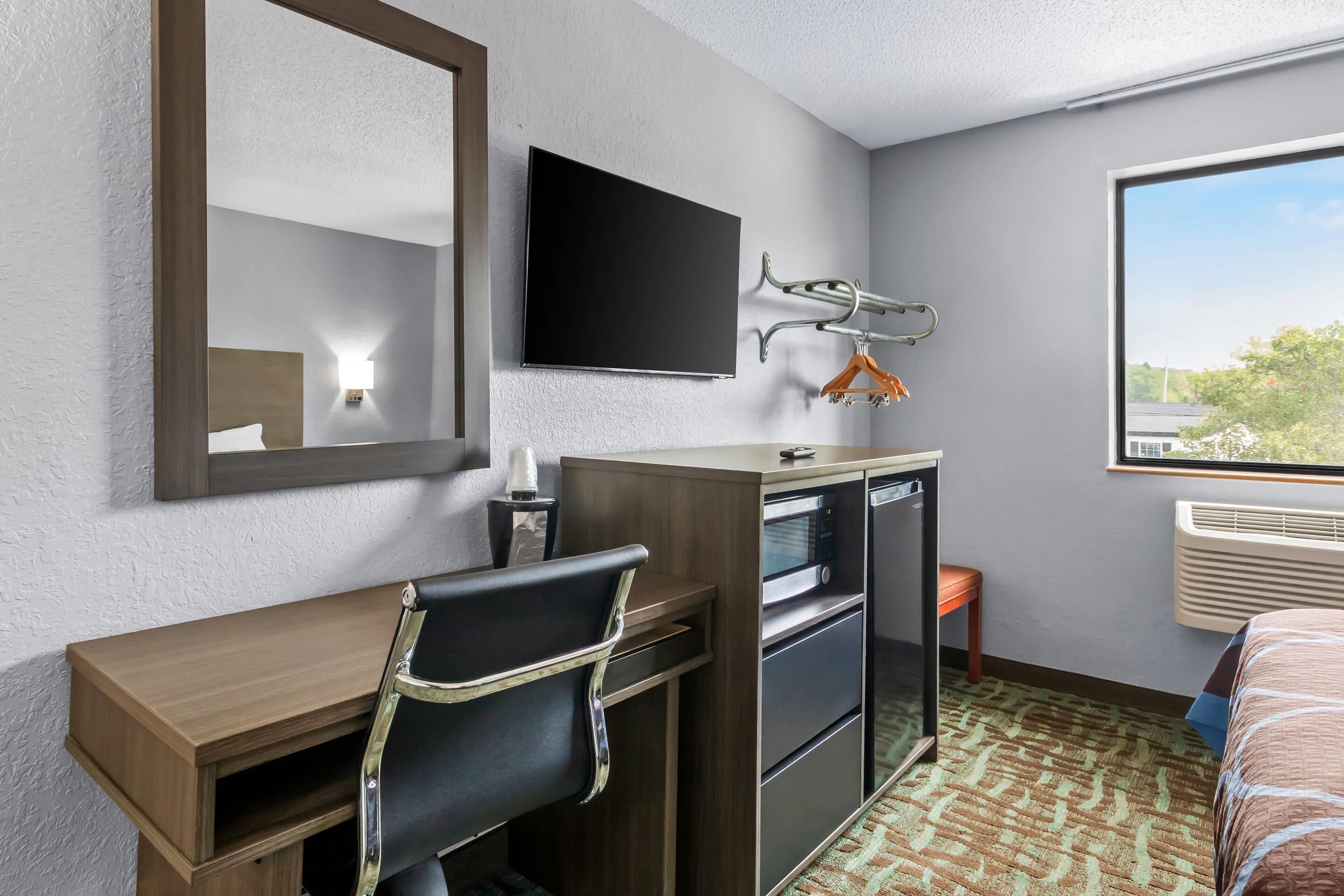 Een hotelkamer met een bed, bureau met stoel, televisie, kapstok, verwarming en raam met uitzicht.