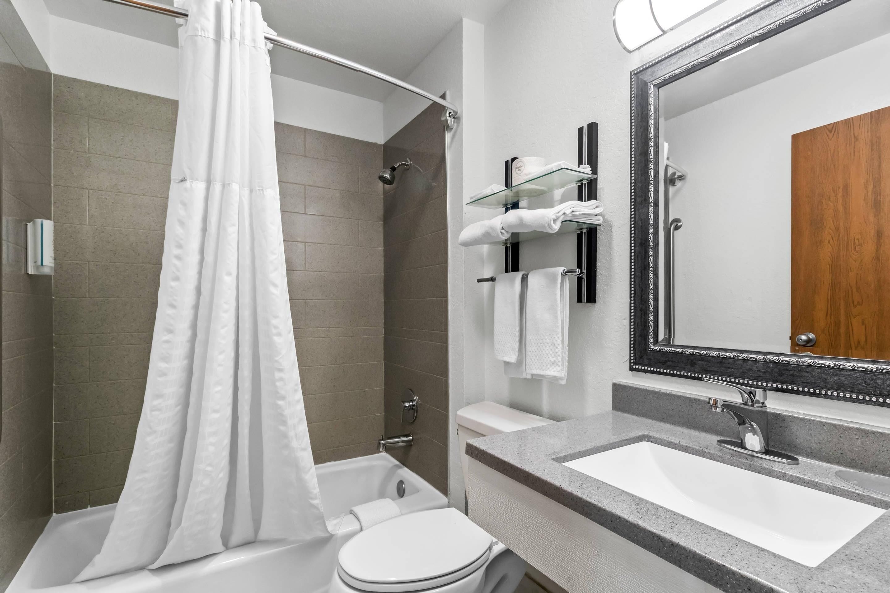 Ein modernes Badezimmer mit Badewanne, Dusche, Toilette und Waschtisch mit Waschbecken und Spiegel.