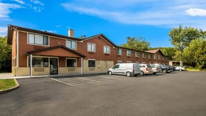 A multi-story building with a parking lot, several parked vehicles, and a clear blue sky. - Rodeway Inn Delmont (Delmont)