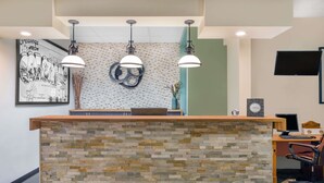 A reception desk with a stone mosaic design, a framed welcome sign, and a modern pendant light fixture. - Travelodge by Wyndham Loveland/Fort Collins Area (Loveland)