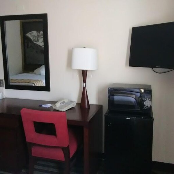 A hotel room with a desk, a red chair, a lamp, a telephone, a television, and a microwave. - Travelodge by Wyndham Loveland/Fort Collins Area (Loveland)