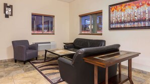 A lobby with a black leather sofa, a gray armchair, a wooden coffee table, and a painting of trees. - Travelodge by Wyndham Loveland/Fort Collins Area (Loveland)