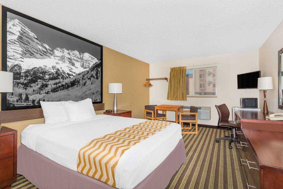 Une chambre d’hôtel équipée d’un lit, d’un bureau, d’une chaise, d’une télévision et ornée d’un grand tableau représentant un paysage de montagne.