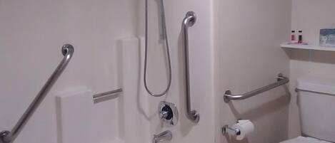A bathroom with a bathtub, a shower, a toilet, and a handrail.