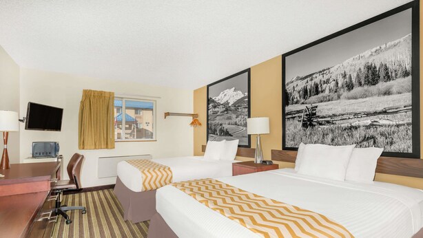 A hotel room with two beds, a desk, a chair, a TV, and large framed pictures on the walls. - Travelodge by Wyndham Loveland/Fort Collins Area (Loveland)