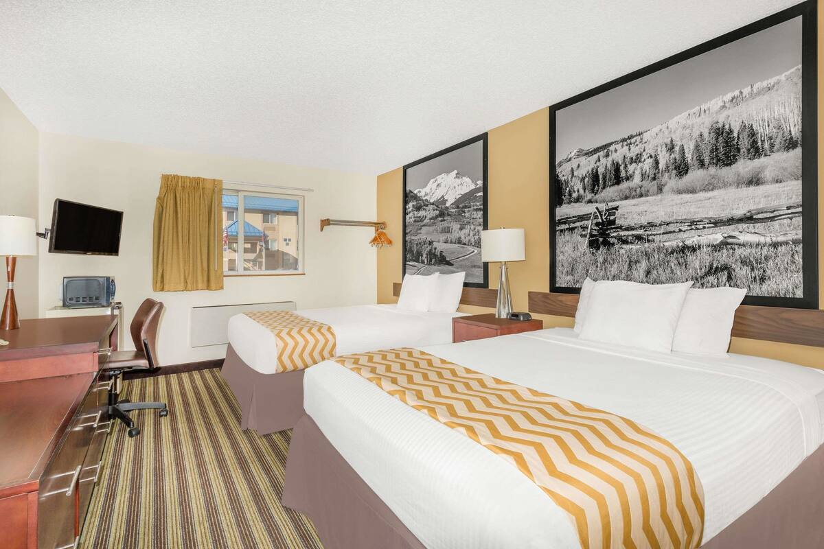 Une chambre d’hôtel avec deux lits, un bureau, une chaise, une télévision et de grandes images encadrées accrochées aux murs.