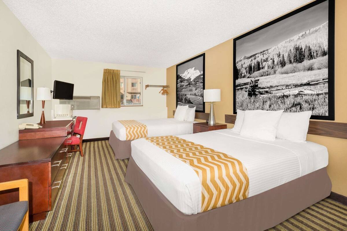 Une chambre d’hôtel avec deux lits, un bureau, une chaise, une télévision et une grande fenêtre.
