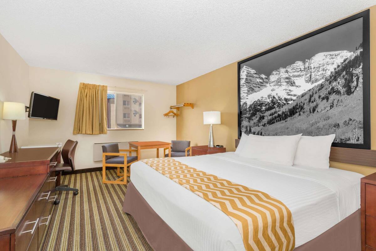 Une chambre d’hôtel avec un grand lit, un bureau, une chaise, une télévision et une vue sur la montagne.