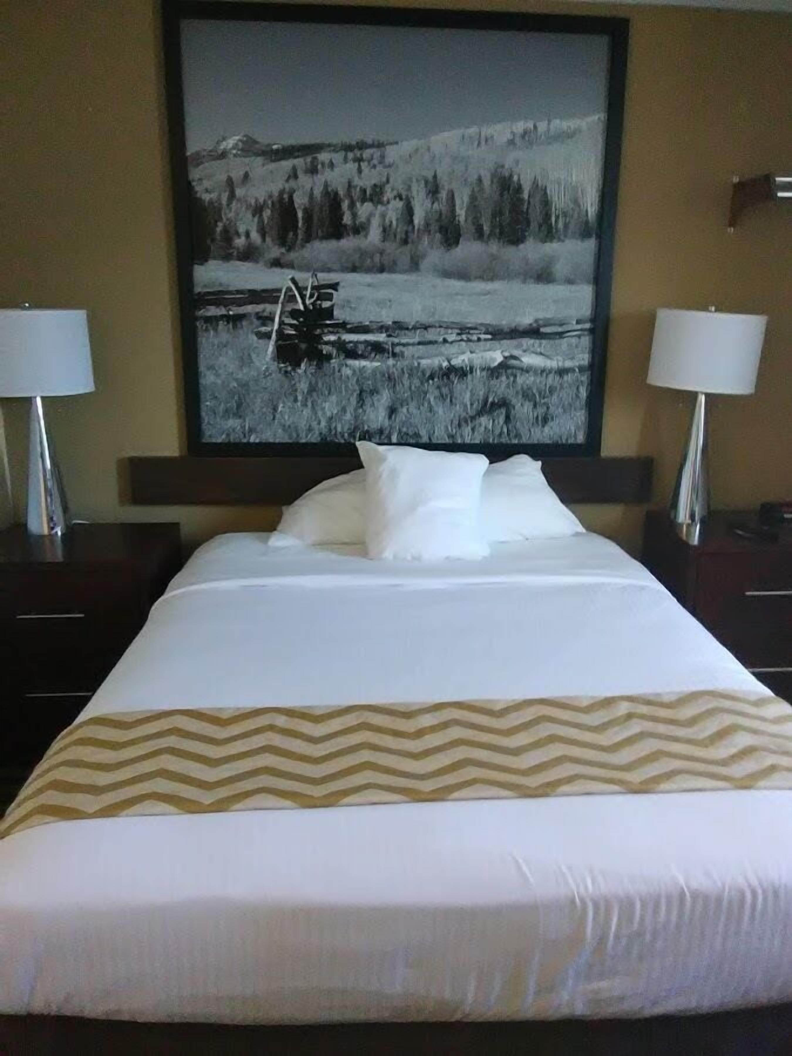 A hotel room with a large bed, two bedside lamps, and a framed landscape painting on the wall.