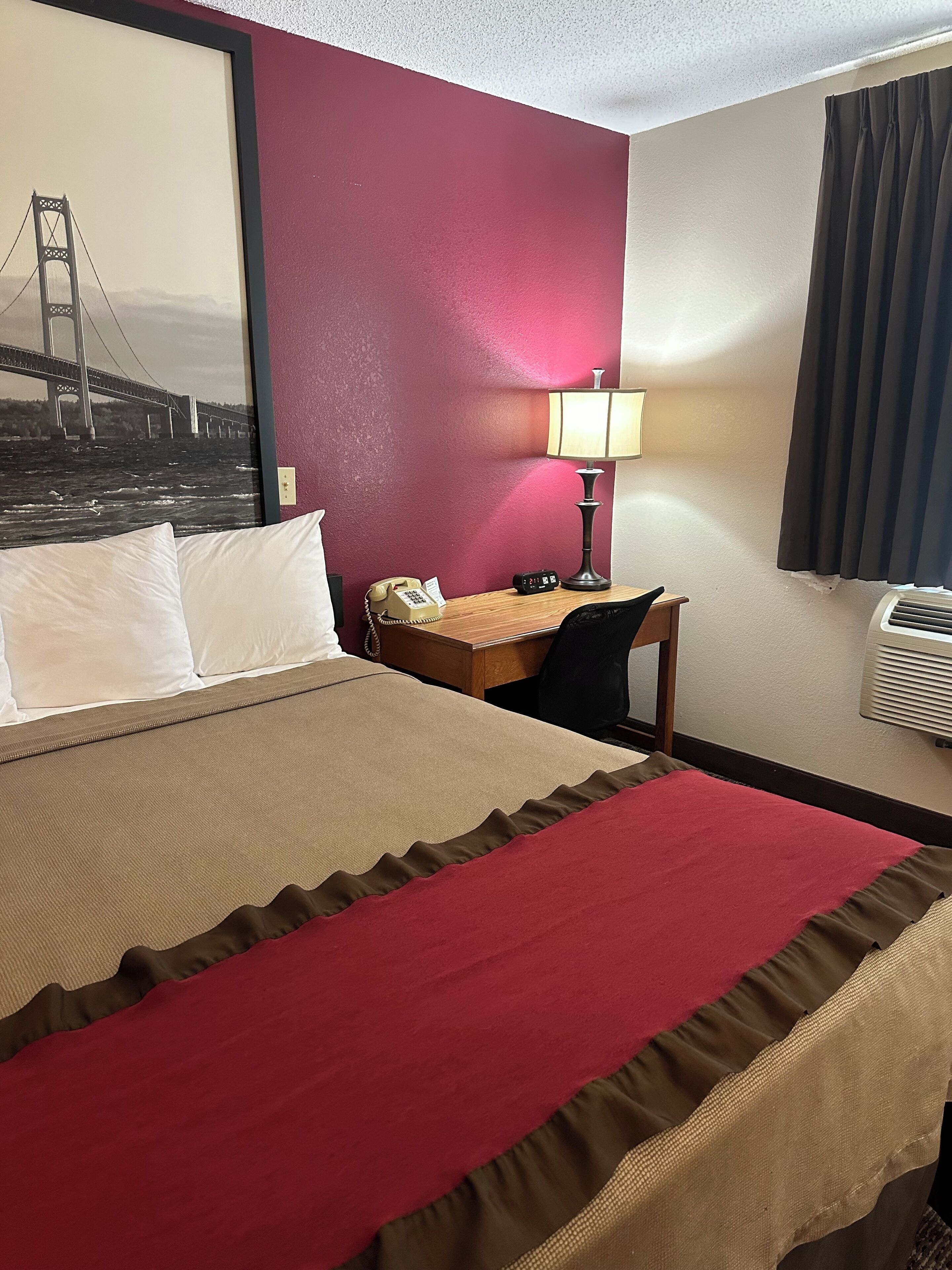 Habitación de hotel con cama, escritorio con lámpara, teléfono y aire acondicionado instalado en la pared.