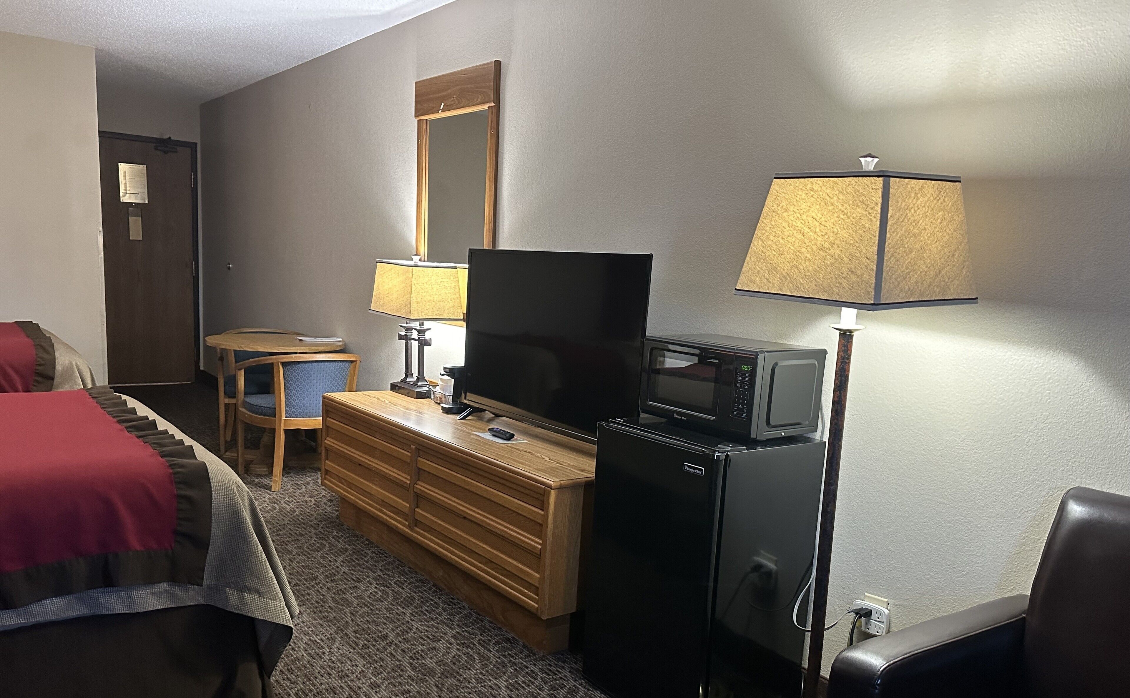 Habitación de hotel con cama, cómoda de madera, televisor, microondas, lámpara y escritorio con silla.