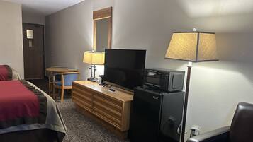 Habitación de hotel con cama, cómoda de madera, televisor, microondas, lámpara y escritorio con silla.