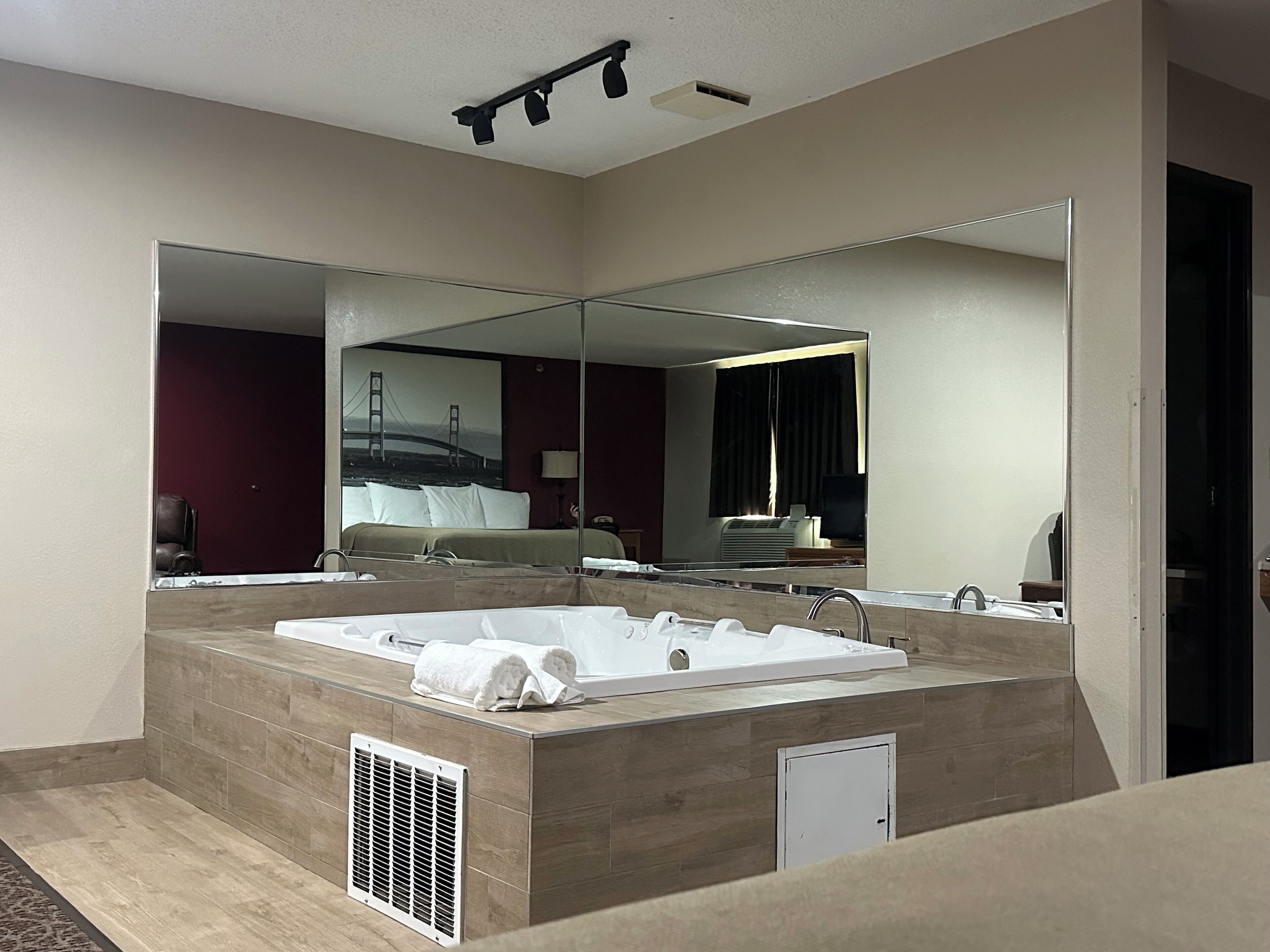 Un baño de hotel moderno con una bañera grande, una ducha a ras de suelo y un espejo amplio.