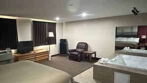 A hotel room with a bed, a desk, a chair, a TV, a lamp, a small table, and a bathtub.