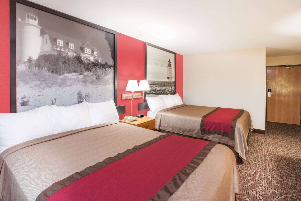 Una camera d'albergo con due letti, un comodino con una lampada e un'ampia foto incorniciata di un faro.