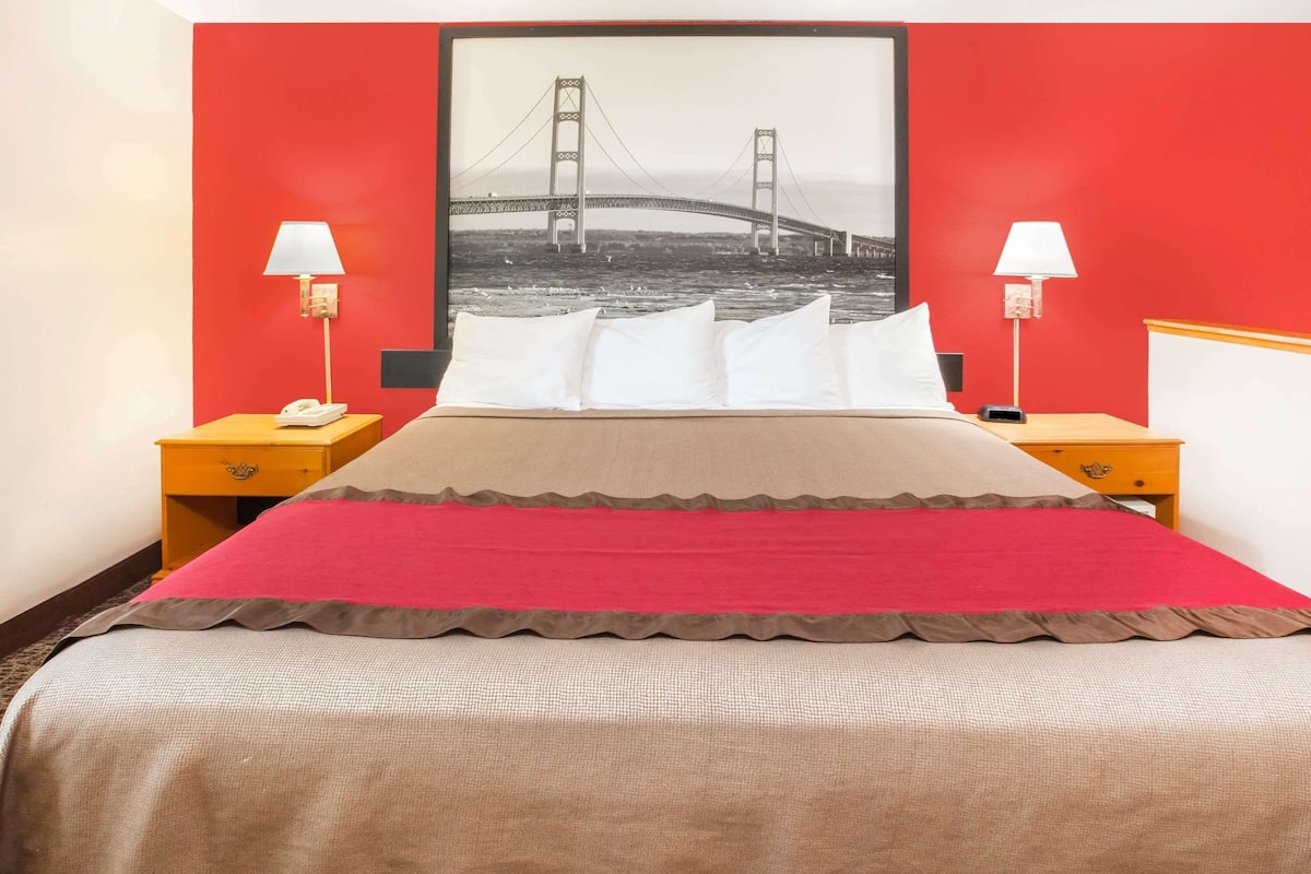Una camera d'albergo con un letto, due comodini, una lampada su ciascun comodino e un grande quadro incorniciato di un ponte appeso al muro.