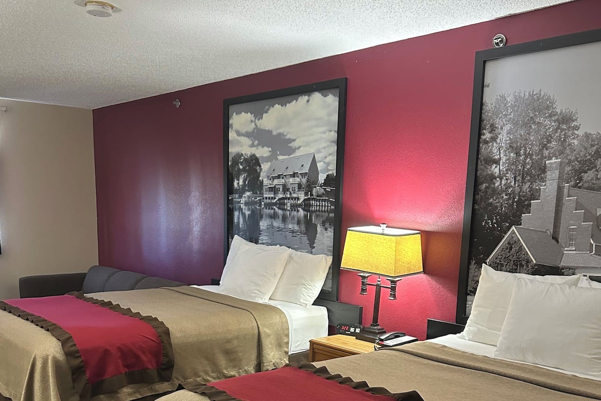 Una camera d'albergo con due letti, ciascuno con copripiumino rosso e beige, un comodino con una lampada e due quadri appesi alle pareti.