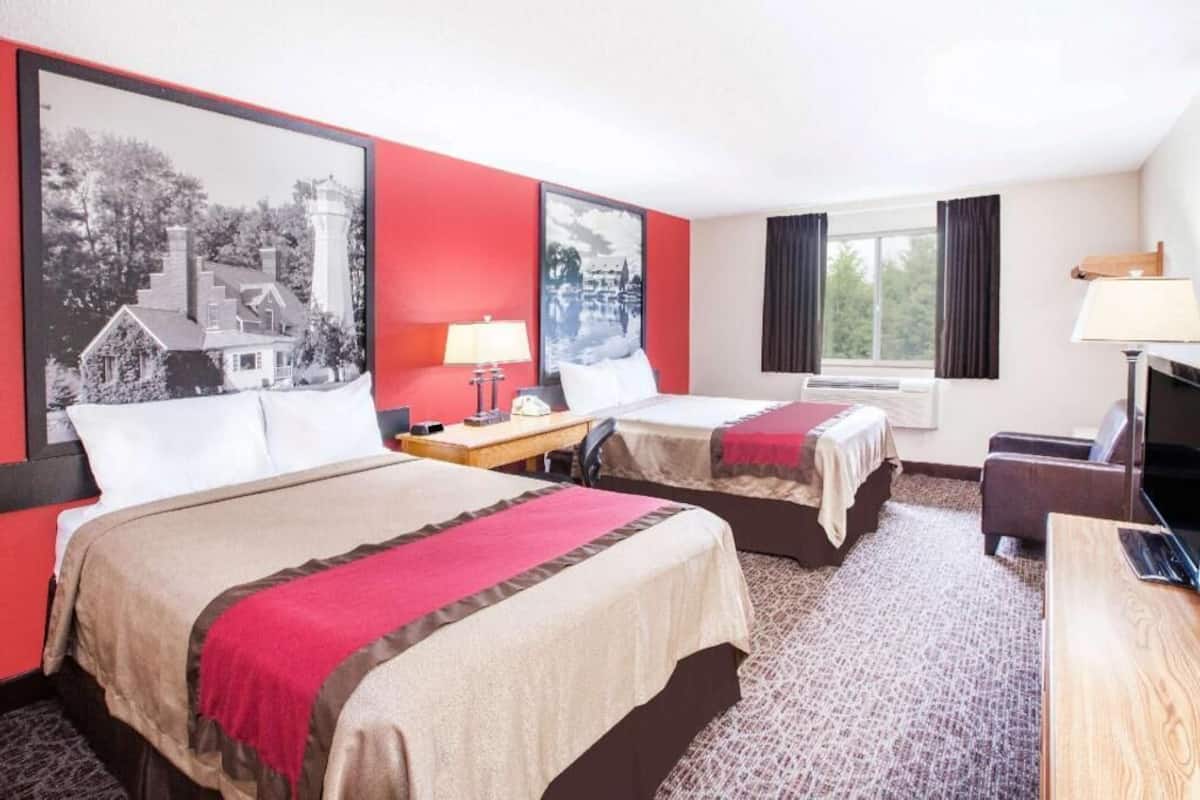 Una camera d'albergo con due letti, una scrivania, una televisione e grandi quadri appesi alle pareti.