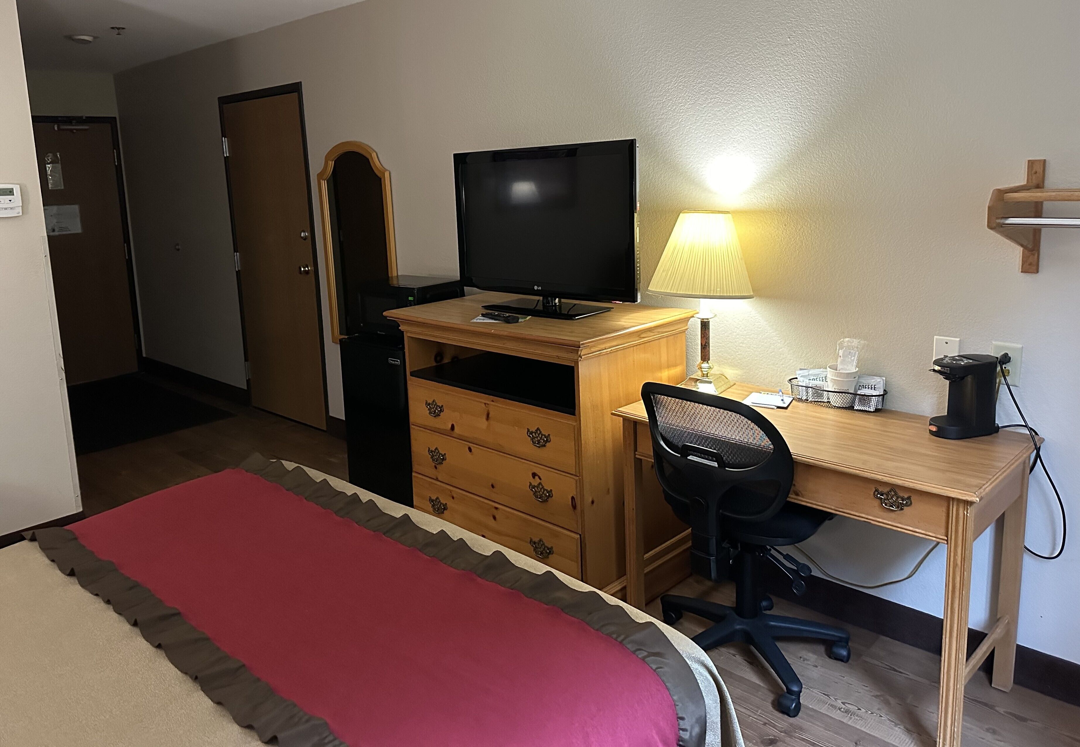 A hotel room with a bed, a desk with a computer, a television, a lamp, and a coffee maker.