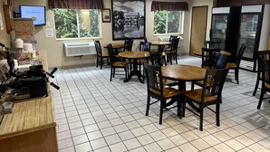 A dining area with multiple tables and chairs, a kitchen area with appliances, and large windows with curtains.