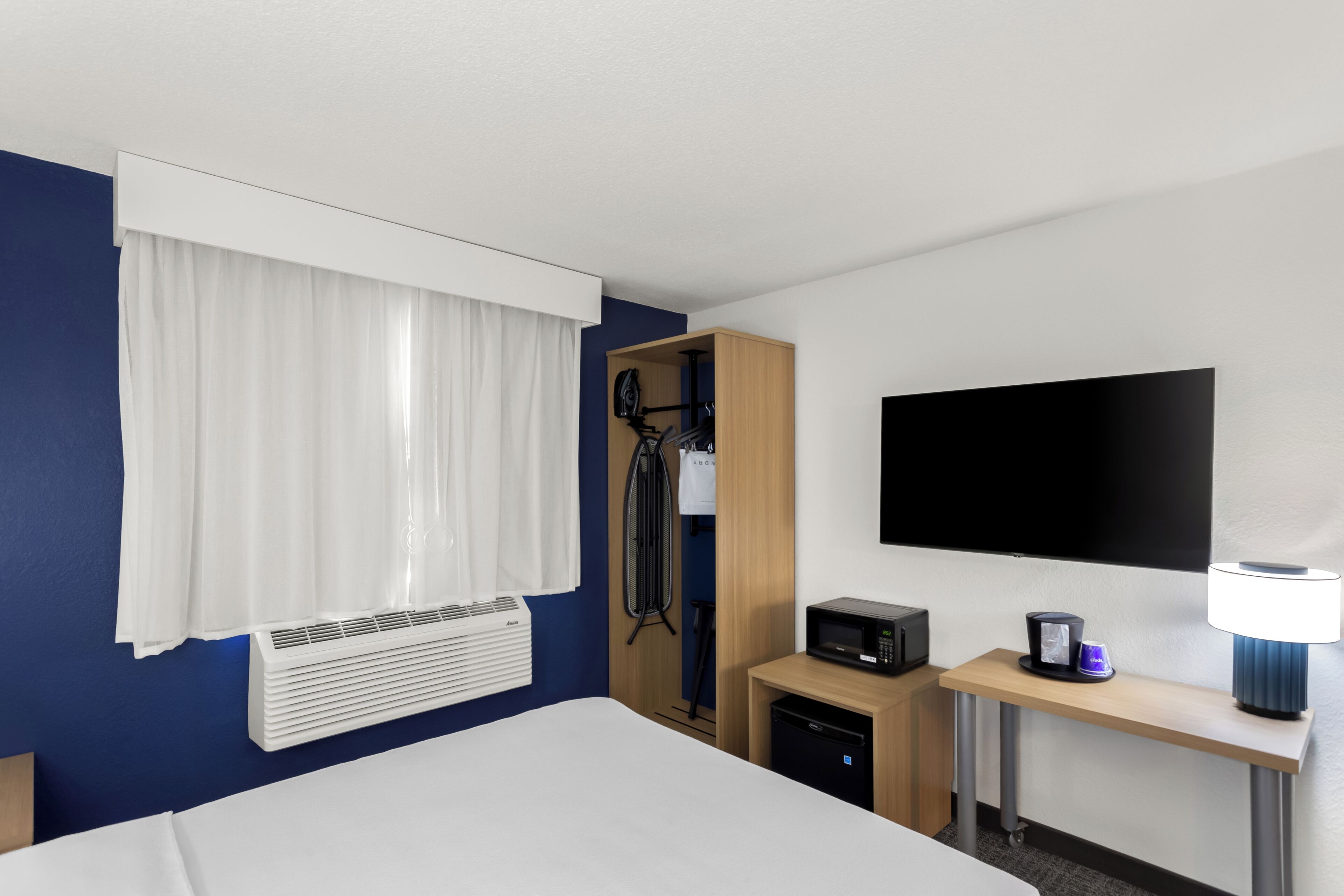 Habitación de hotel con cama, escritorio con lámpara, televisión, microondas y calefacción.