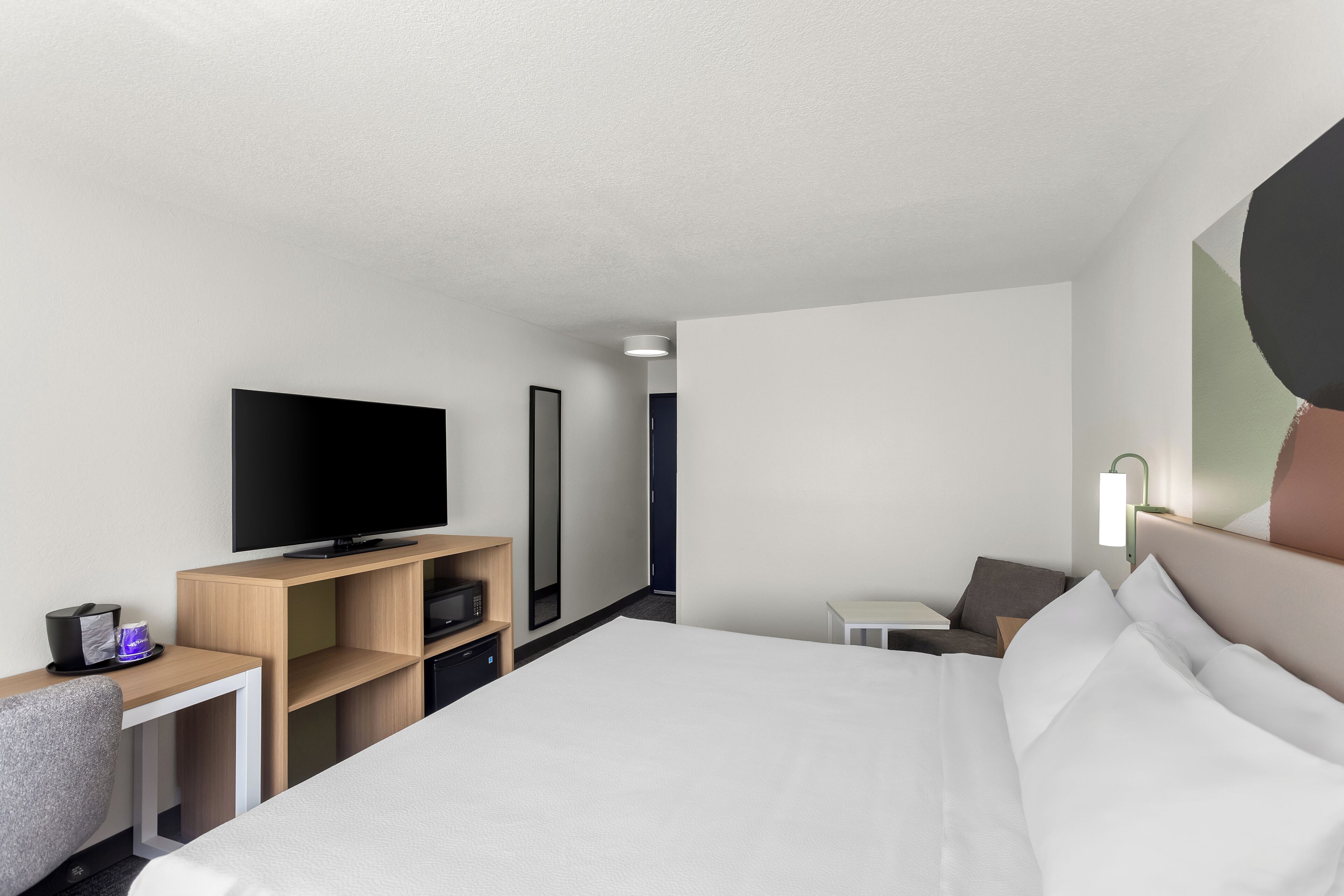 A hotel room with a bed, a TV, a desk, and a chair.